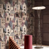 Carta da parati GAIA con villaggio stilizzato nei toni beige, bordeaux e antracite, in ambientazione elegante con lampada da terra e oggetti decorativi