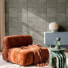 Carta da parati geometrica effetto tessuto TRAMA in soggiorno moderno con poltrona terracotta e tavolino verde.